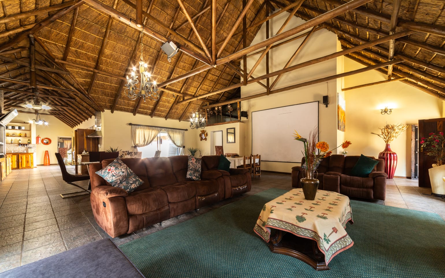 Spacious communal lounge with brown sofas, high thatch ceilings and warm lighting
